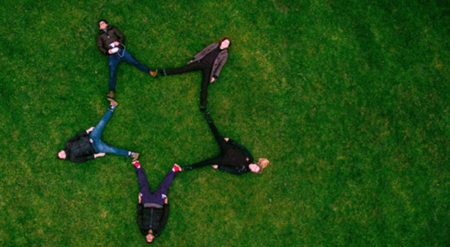Cinq personnes allongées sur l’herbe ; leurs pieds et jambes sont écartés pour former une étoile, Photo de Oxford University Parks, Oxford, United Kingdom, Sidharth Bhatia, sous la Licence Unsplash
